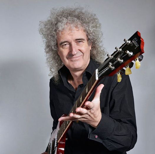 Guitarist holding a red electric guitar with three tuning pegs on each side of the headstock