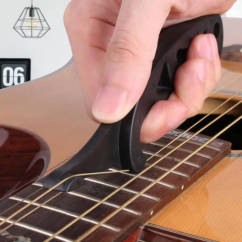 Hand using a black guitar string stretcher on an acoustic guitar fretboard